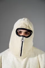 Canguro de peluche color crema, con cuello alto y cierre frontal parcial. Presenta un parche ovalado con diseño gráfico en el pecho y un bolsillo frontal tipo canguro.
