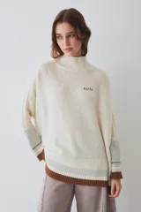 Buzo tejido de silueta amplia con cuello alto, mangas largas con detalle de trenzado y puños acanalados en contraste. Presenta bordado de la marca en el pecho y diseño de rayas en el ruedo y los puños.