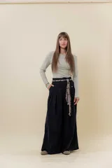 Pantalón wide leg de tiro alto en color negro, con diseño de pinzas delanteras que aportan volumen y caída fluida. Incluye bolsillos laterales y un lazo desmontable en la cintura que combina cordón con cinta de estampado animal print.