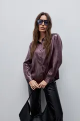 Camisa blanca de calce relajado con acabado satinado y brillo sutil, cuello clásico, cierre frontal con botones y mangas largas con puños.
