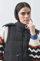 Chaleco puffer negro con diseño acolchado, capucha desmontable y cierre frontal. Cuenta con cordones ajustables en la cintura y bolsillos laterales.