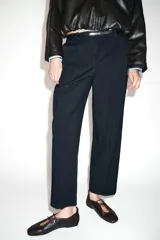 Pantalón tobillero de corte recto en color beige, con detalle de nervio delantero marcado. Incluye cinturón fino, bolsillos delanteros y cierre frontal con cremallera, botón interior y gancho.