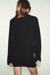 Vestido corto de punto con cuello subido, manga larga y sisa ancha. Presenta un detalle de costura vertical marcada en el centro del delantero y acabados en rib en cuello, puños y ruedo.