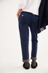Pantalón recto de tiro medio confeccionado en pana con lycra. Presenta pinzas frontales, bolsillos laterales y traseros, y cierre con botón dorado. El diseño destaca por el detalle de paño espigado en el interior del ruedo, visible al doblarlo, y un pin bordado decorativo en el bolsillo delantero.