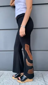 Pantalón negro de tejido de punto con corte acampanado y apliques de cuero sintético color cobre en la parte inferior de las piernas.