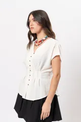 Blusa beige melange con escote en V, manga corta caída, botones metálicos frontales y pinzas que marcan la cintura.