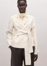 Chaqueta de mezcla de lana, poliéster y elastano color marfil, con solapas cruzadas, cuello alto y cinturón ajustable del mismo tejido. Cuenta con mangas largas y forro interior de viscosa.