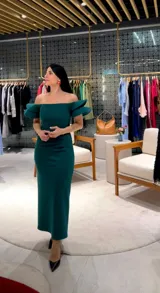 Vestido midi de fiesta color verde esmeralda, con escote recto estilo bardot y mangas cortas con volados estructurados. Presenta un corte ajustado al cuerpo con detalle de fruncido lateral en la cintura.