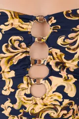 Malla enteriza de color azul marino con estampado barroco en tonos beige y dorado. Presenta un escote recto con tirantes finos, aberturas frontales unidas por argollas metálicas y laterales fruncidos.