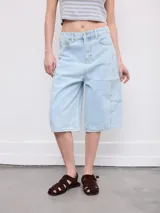 Bermuda de jean de tiro alto, color celeste claro, con diseño amplio y largo por debajo de las rodillas. Cuenta con bolsillos clásicos y costuras pespunteadas en contraste.