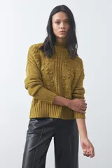 Polera de tejido de punto color marrón, con cuello alto y diseño de textura con relieves y trenzas. Posee mangas largas con puños acanalados.