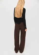 Jersey de punto fino acanalado en color negro, con cuello redondo y manga larga. Presenta un diseño entallado con bajo asimétrico y detalle de botones laterales decorativos.