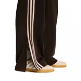Pantalon deportivo adidas modelo Firebird Loose, color marrón oscuro con las icónicas tres tiras laterales en color crema. Presenta corte holgado, cintura elástica y logo del trébol bordado en la pierna.