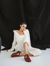 Sandalia cerrada tipo pescador, color blanco o hueso brillante, con tiras entrecruzadas en el empeine y cierre de hebilla ajustable en el lateral. Posee suela y taco bajo de color negro.