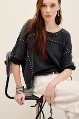 Remera de algodón negro con efecto deslavado, cuello redondo y mangas cortas. Presenta aplicaciones de tachas metálicas en el escote, hombros y a lo largo del frente.