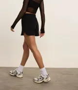 Bermuda deportiva femenina modelo runner, color negro, con cintura elástica ajustable con lazo, bolsillos laterales y aberturas laterales. Confeccionada en tejido de media malla.