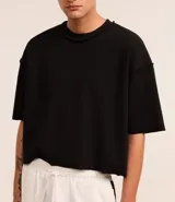 Remera negra de algodón con corte oversized, cuello redondo y manga corta. Presenta un tejido acanalado y un dobladillo sin rematar.