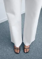 Jeans blancos de tiro alto con diseño acampanado y bajo deshilachado, con cierre de cremallera y botón, trabillas para cinturón y bolsillos traseros.