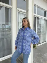 Camisa de corte holgado en color azul con bordado floral blanco tipo broderie. Presenta cuello clásico, cierre frontal con botones y mangas largas abullonadas con puños ajustados.