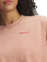 Remera Under Armour de corte cropped y estilo relaxed, en color rosado con efecto lavado, cuello redondo acanalado y mangas cortas amplias. Presenta un pequeño parche con el logotipo de la marca en el pecho.