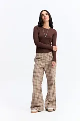 Pantalón de tiro medio con corte recto y leve apertura en el bajo. Presenta un diseño de estampado a cuadros en tonos beige y marrón.