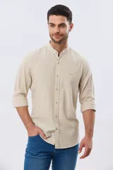 Camisa de lino y algodón color beige, de manga larga, con cuello mao y cierre frontal con botones. Presenta un pequeño bordado al tono en el pecho.