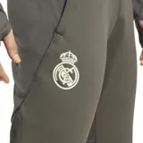 Pantalón de entrenamiento Adidas del Real Madrid, modelo Tiro 25. Color verde oliva con logo Adidas y escudo del club en color claro. Corte ajustado, cintura elástica con cordón, bolsillos con cierre y tecnología AEROREADY. Confeccionado en poliéster reciclado.