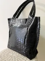 Cartera tipo shopper de cuero genuino marrón, con terminaciones artesanales trenzadas en las asas y los laterales, bolsillo frontal externo y asas largas para llevar al hombro.