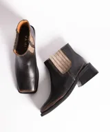 Bota corta tipo chelsea de cuero vacuno color negro, con puntera cuadrada, taco cuadrado de madera y detalle de textura grabada en el panel elástico lateral.