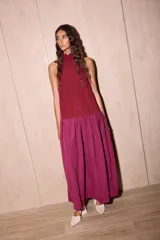 Vestido largo holgado de dos tonos de bordó/fucsia, con escote halter y cuello alto con volado. Presenta un corte en la cadera que da lugar a una falda con maxi volado.