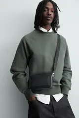 Bandolera negra con textura grabada, compartimento principal con cierre de cremallera, bolsillo interior con cremallera, bolsillo plano frontal, asa de hombro ajustable y extraíble.