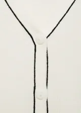 Cardigan de punto canalé color blanco, con cuello en V y cierre frontal de botones. Presenta un diseño ajustado con ribetes en contraste negro en el cuello y la botonera.