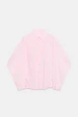 Camisa de algodón de corte oversize, color rosa claro, con cuello solapa, manga larga con puños y cierre frontal con botones. Presenta detalles de pliegues en el delantero.
