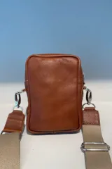 Bandolera pocket bag de cuero vacuno color suela, con bolsillo frontal con cierre y detalle de placa metálica con logo. Cuenta con correa de cinta ancha regulable y herrajes metálicos plateados.