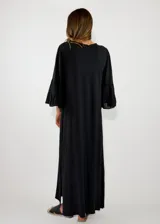 Vestido largo negro de corte holgado, con escote en V y mangas largas con volados en los puños.