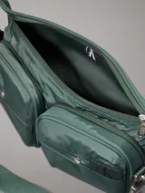 Riñonera verde militar de poliéster reciclado, con correa ajustable con clip, cierre de cremallera, dos bolsillos exteriores con anillas en D y logo de Calvin Klein en el frente. Se pliega y se cierra con cremallera para crear una cartera de muñeca.