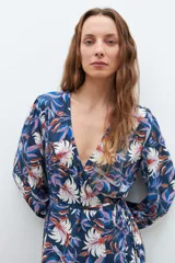 Maxi vestido azul marino con estampado floral en tonos blanco, rosa y azul. Diseño cruzado con lazo en la cintura y mangas largas.