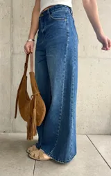 Jean wide leg de tiro medio-alto, color azul con lavado clásico y efecto desgastado. Presenta costuras laterales destacadas que estilizan la silueta, bolsillos delanteros y traseros, y cierre frontal con botón metálico y cremallera.