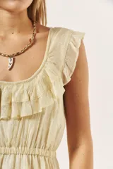 Vestido corto color crema con acabado brillante, escote redondo con volados decorativos en los hombros, cintura elástica y falda acampanada.