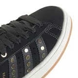 Zapatillas Adidas modelo Campus 00s, de corte bajo, color negro con detalles en dorado. Presentan capellada de gamuza, las tres tiras laterales perforadas con tachas doradas y la palabra "CAMPUS" estampada en dorado. La suela es de goma color crema con una banda de goma color caramelo en la base.