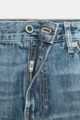 Jeans de tiro medio con corte bootcut, confeccionados en denim azul con efecto lavado y ligeros desgastes. Presentan diseño de cinco bolsillos, trabillas en la cintura y cierre frontal con cremallera y botón.