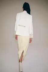 Chaqueta de estilo militar de ZARA Woman Collection, confeccionada en mezcla de algodón en color blanco y beige. Presenta cuello subido, manga larga con puños anchos en contraste y cierre frontal con alamares y botones metálicos en relieve. Tiene bajo asimétrico con abertura en la espalda.