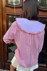 Camisa de lino texturado con diseño a rayas verticales rojas y blancas, cuello babero desmontable en color lila con volados y mangas cortas abullonadas.