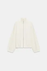 Chaqueta de punto color crudo con cuello alto, cierre frontal de cremallera metálica, mangas largas con puños elásticos y bajo ajustable con cordones.