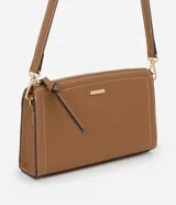 Cartera bandolera pequeña de formato rectangular, confeccionada en poliuretano color tostado con costuras decorativas en contraste. Cuenta con cierre superior de cremallera con tirador alargado, placa metálica frontal con logo y correa larga ajustable y desmontable mediante mosquetones.