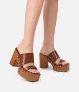 Sandalia de tacón alto y plataforma, color marrón, con punta cuadrada, dos tiras en el empeine decoradas con tachuelas doradas laterales y suela con acabado efecto madera.