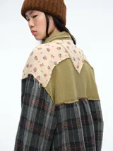 Camisa de corte oversize con diseño patchwork que combina paneles de tela a cuadros en tonos oscuros con paneles superiores de tela beige con estampado floral. Presenta cierre frontal con botones, cuello clásico y bolsillos delanteros con solapa.