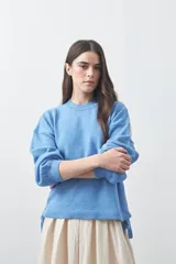 Sweater de tejido liviano con silueta relajada, hombros caídos y mangas largas con puños ajustados. Presenta cuello redondo y lazos ajustables en el bajo.