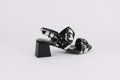 Sandalias negras de cuero charol con dos tiras, una sobre los dedos y otra sobre el empeine, ambas con apliques de tachas plateadas. Tira trasera con hebilla. Taco cuadrado.