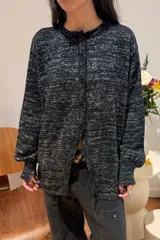 Camisa de punto con acabado brillante, color negro con destellos plateados, diseño de rombos, cuello redondo, cierre frontal con botones y mangas largas con puños ajustados.
